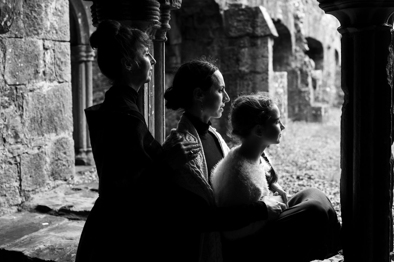A black and white photograph shows three people sitting in silhouette against a stone archway in an old building.