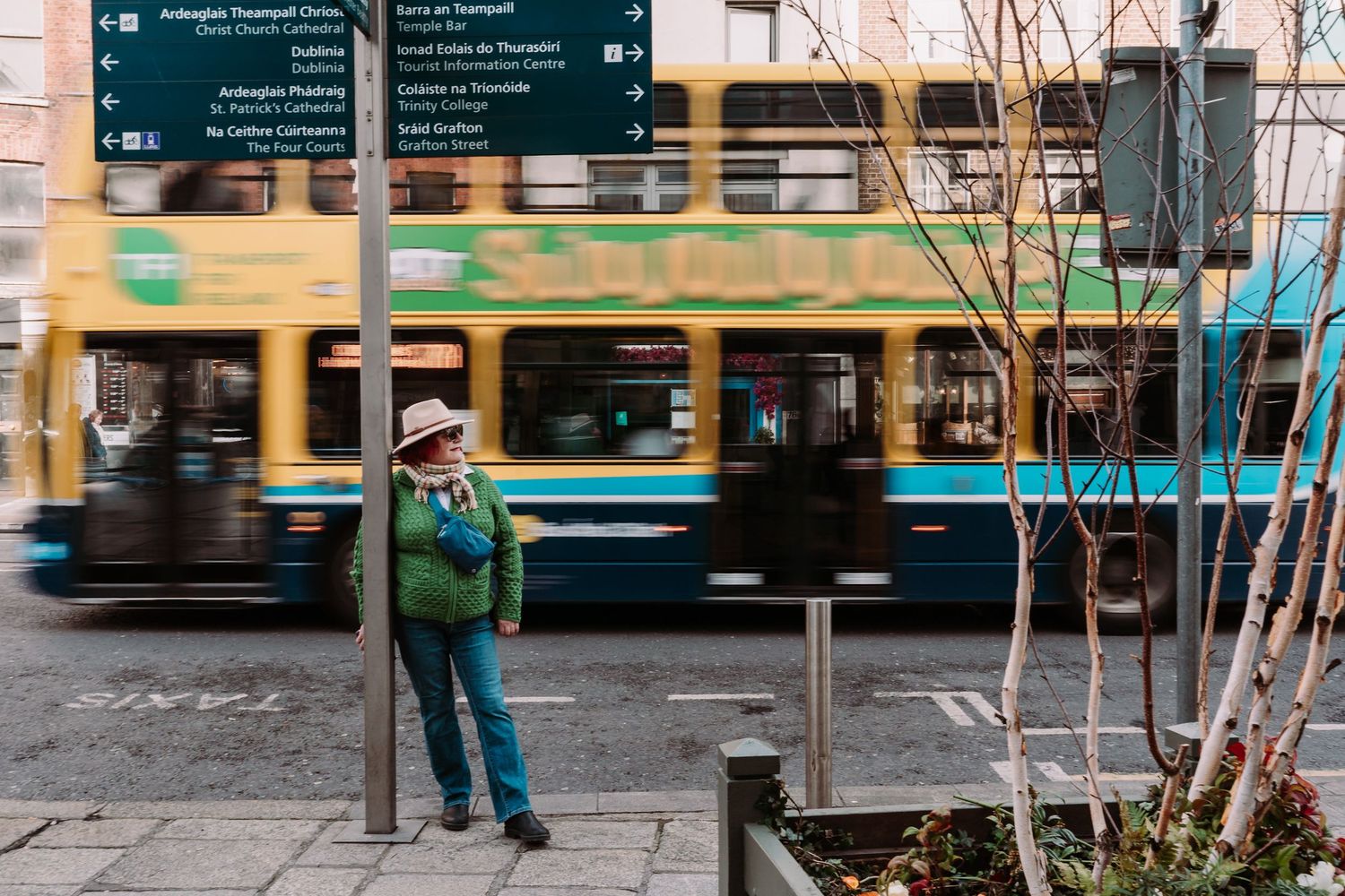 A commuter waits at a tram stop in the city as a blurred yellow streetcar passes by in motion.