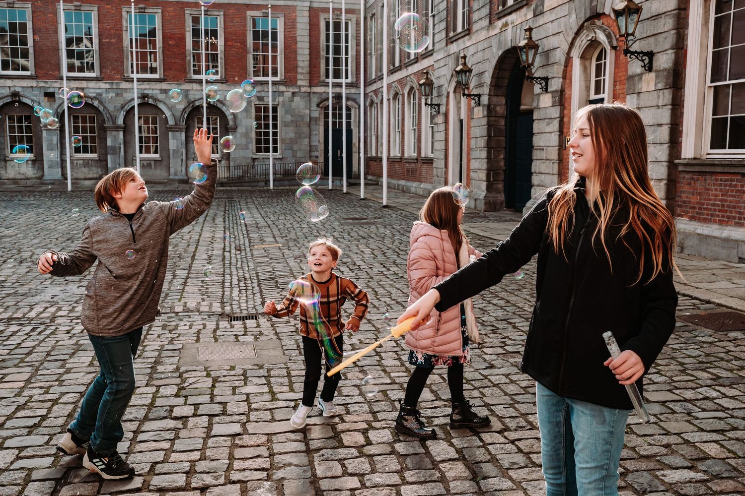 A family dances and plays together on a cobblestone street outside historic brick buildings in an urban setting.