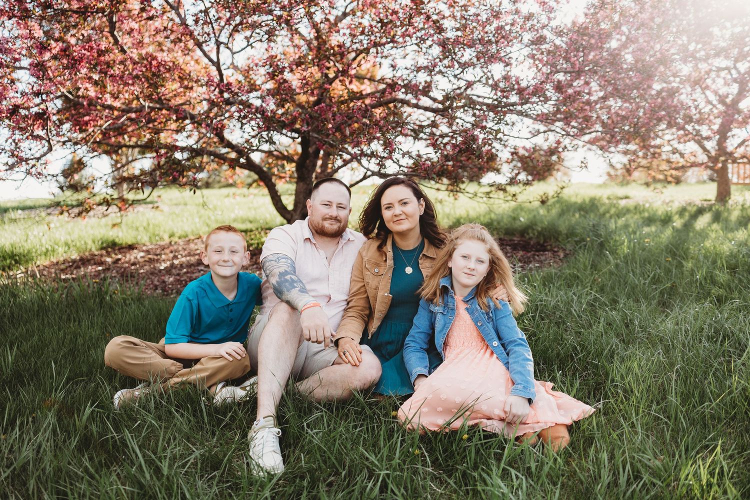 A group relaxes together under a blooming cherry blossom tree on a sunny spring day in a grassy field.