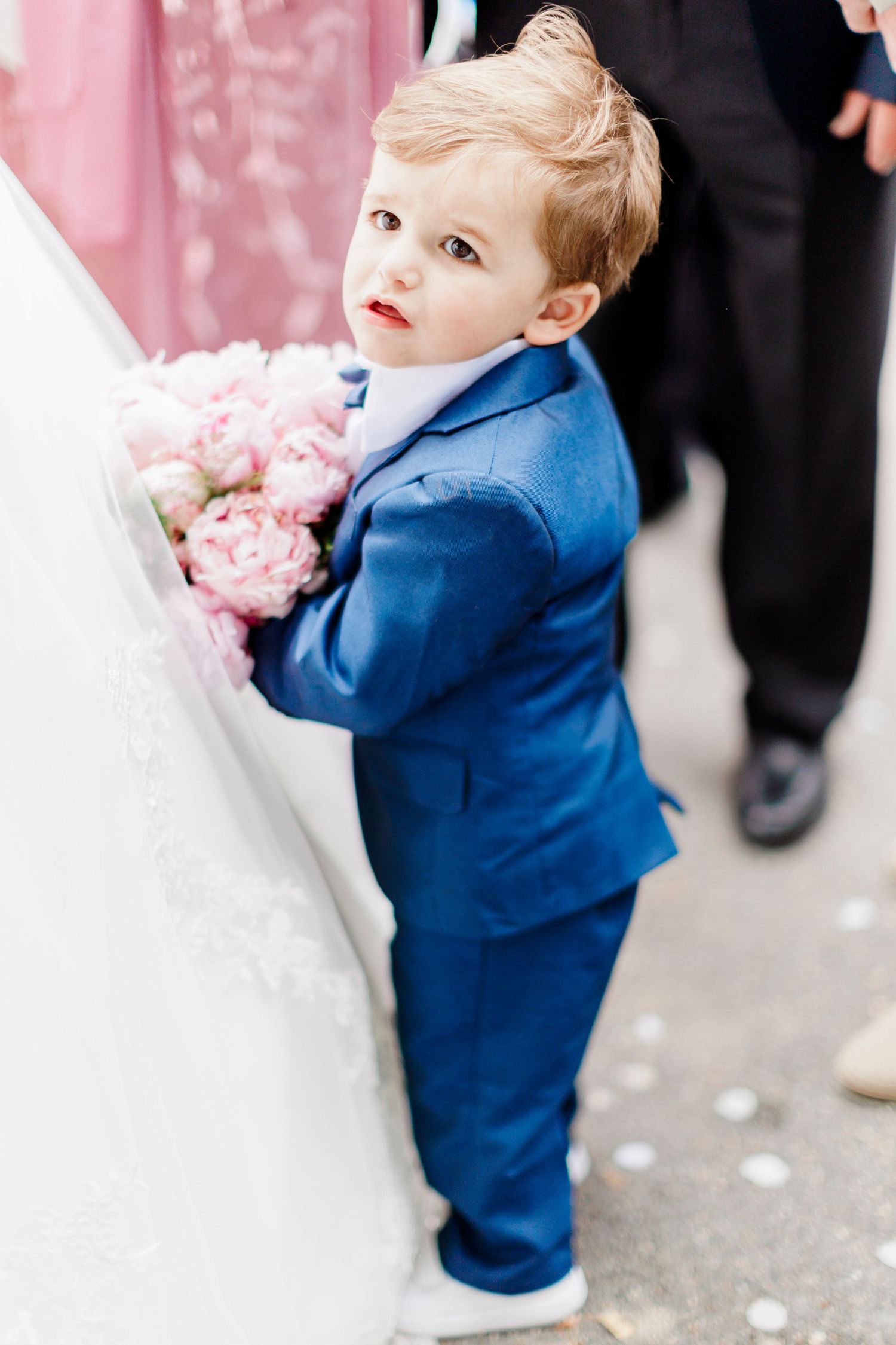 A young child in a blue suit stands next to flowing white fabric.