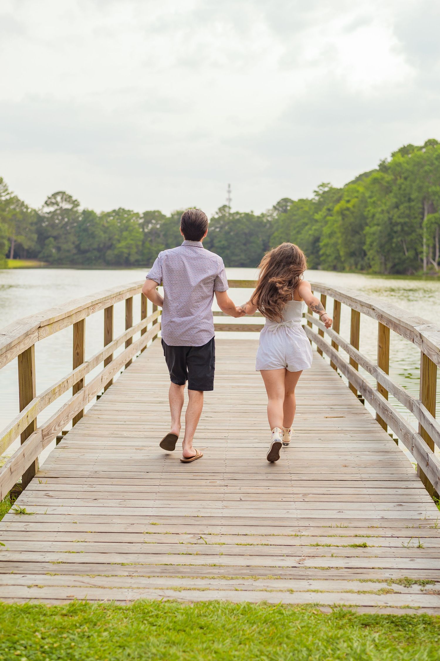Couple walking hand in hand on wooden pier overlooking scenic lake.