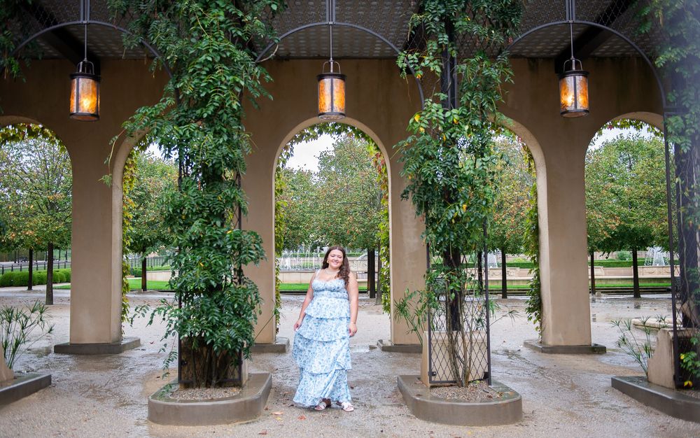 Elegant archway with hanging lanterns and climbing vines creates a romantic garden atmosphere in a park setting.
