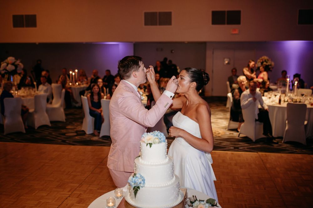 Wedding couple sharing cake at their reception with purple ambient lighting.