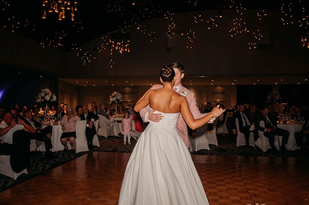 Same-sex couple dancing intimately in white dresses during their wedding reception.