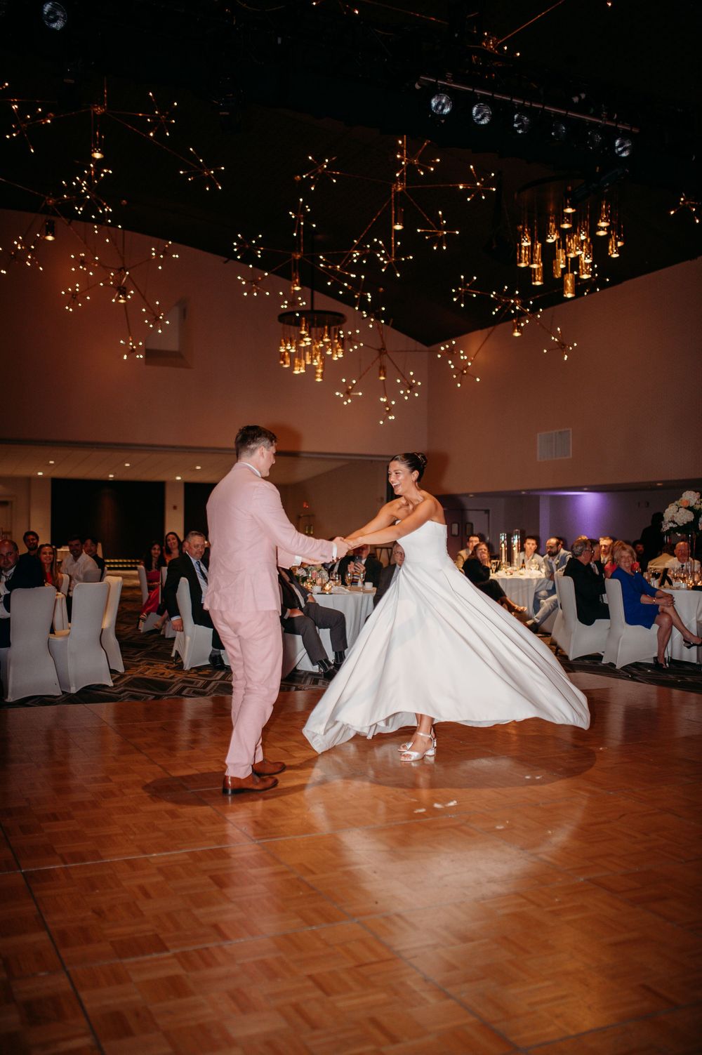 Wedding dancers perform coordinated moves on a parquet floor under twinkling lights.