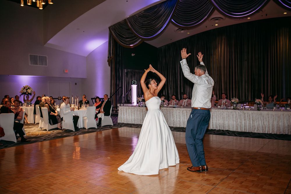 Couple performs choreographed dance moves on wooden dance floor at wedding reception.