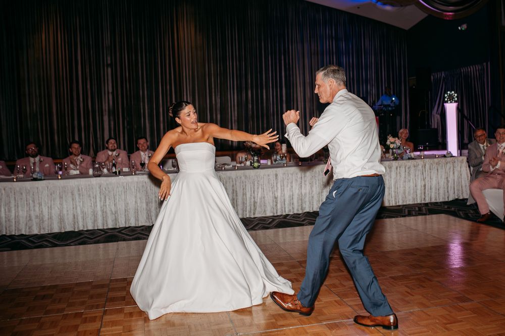 A newlywed couple shares a playful dance moment on the wedding reception dance floor.
