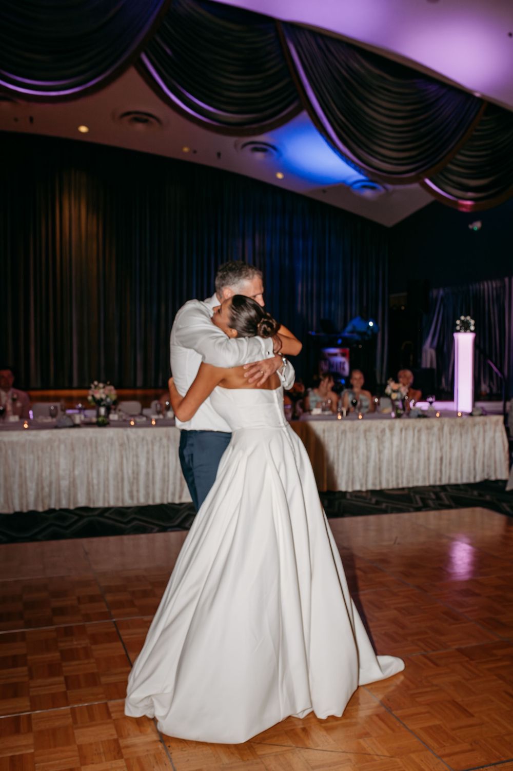Wedding couple embraces during a romantic dance at their reception with purple lighting.