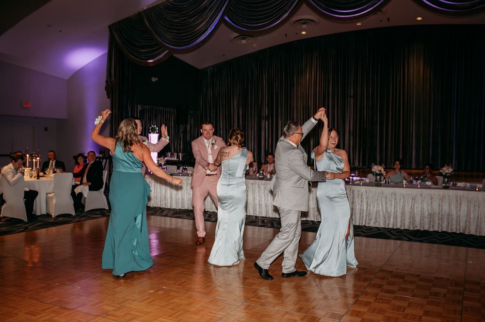 Reception guests dance and celebrate on a wooden dance floor at an elegant wedding venue with colored lighting.