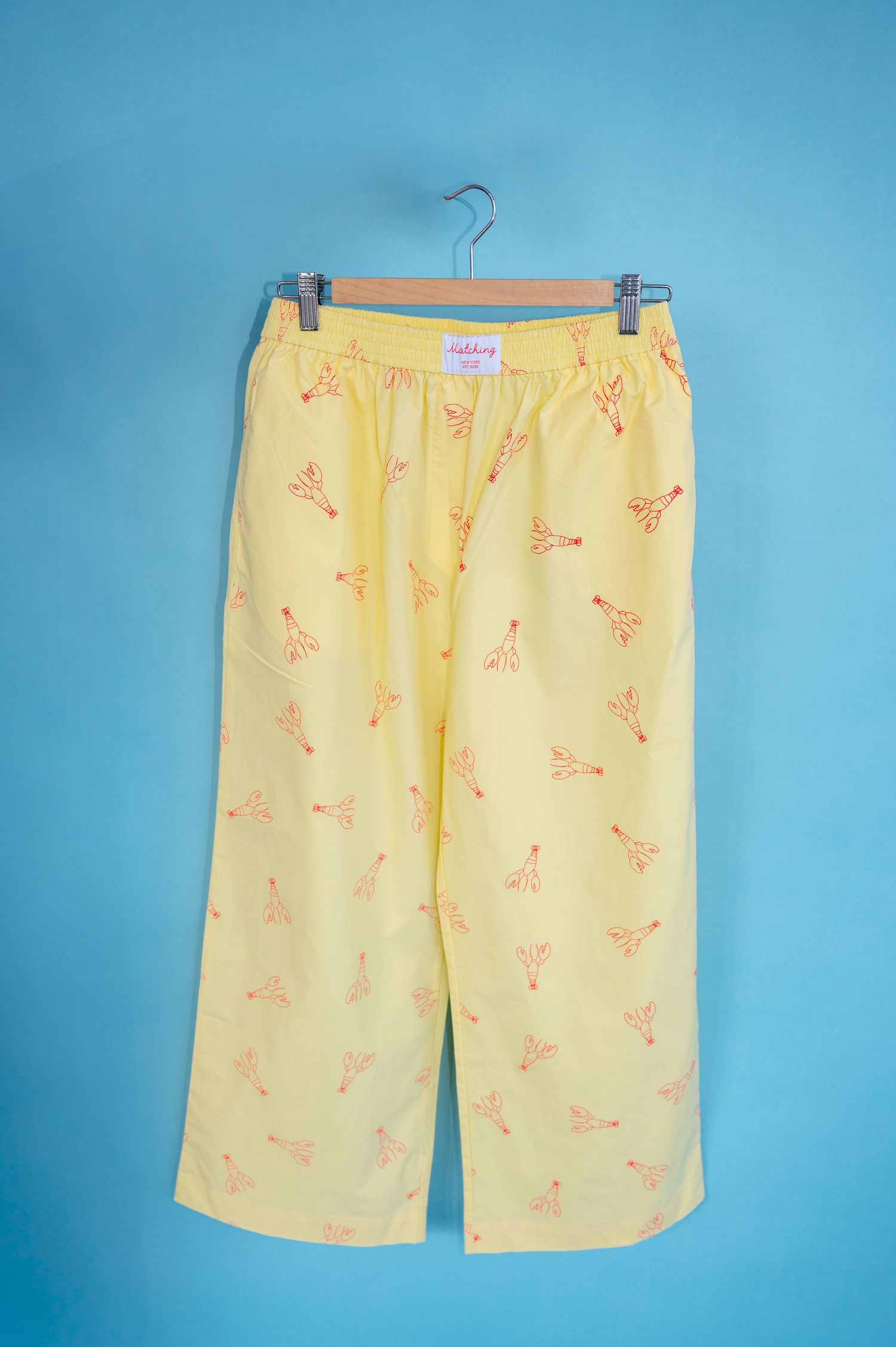 Yellow swim shorts with coral-colored bird pattern displayed on blue background from multiple angles.