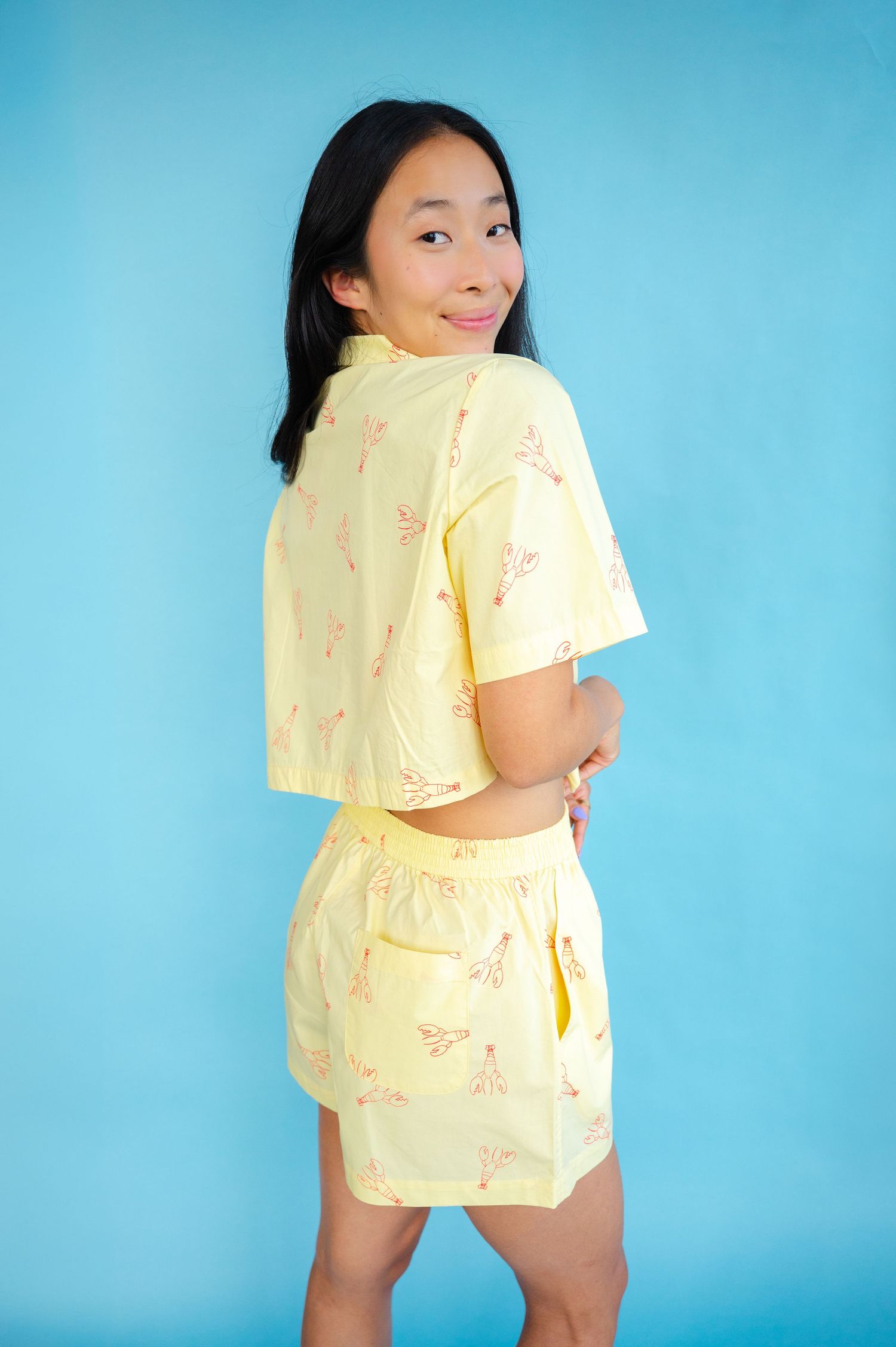 Someone poses wearing a light yellow two-piece shorts set with a fun print against a bright blue background.