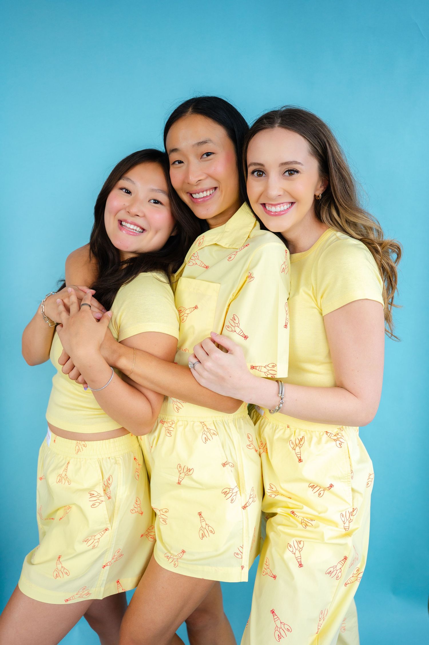 Three people in matching yellow tops pose playfully together against a bright blue studio backdrop.