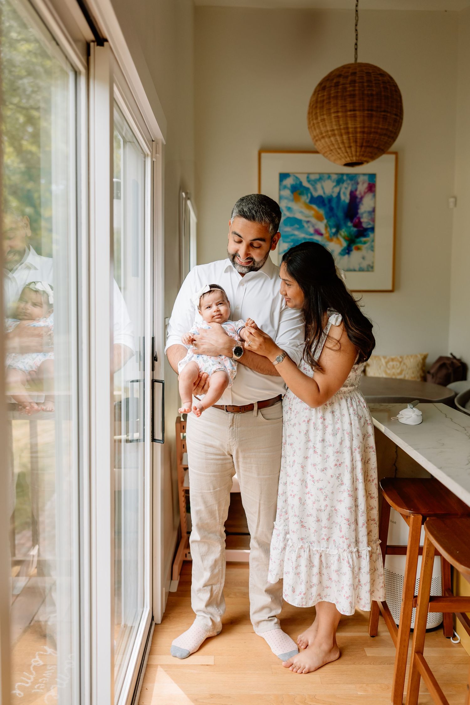 A cozy family moment by large windows with a woven pendant light and colorful wall art in a bright modern home.