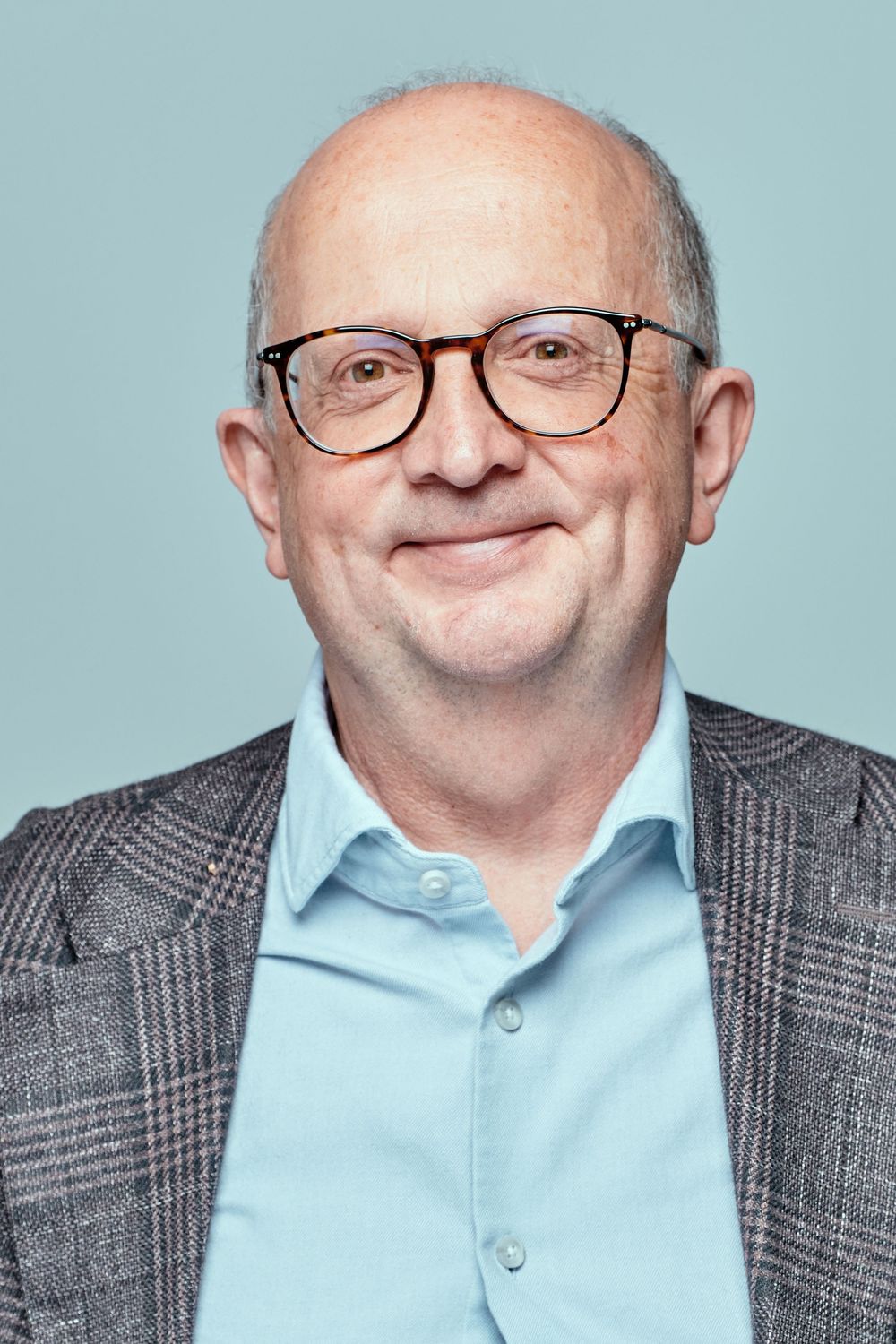 Professional headshots showing a smiling person in glasses wearing a light blue shirt and grey plaid blazer.