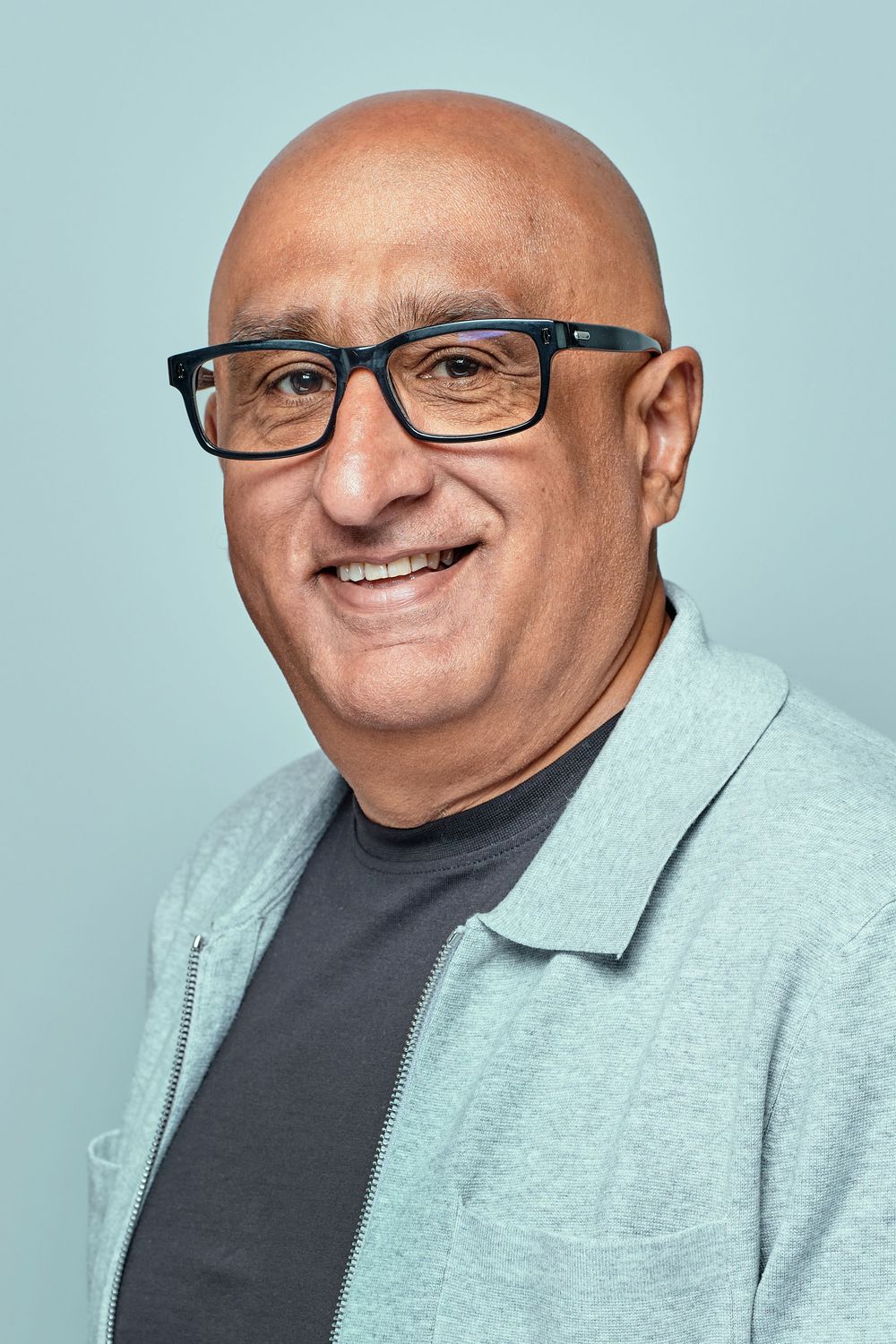 Professional headshot of a smiling person wearing black-rimmed glasses and a light blazer against a blue background.
