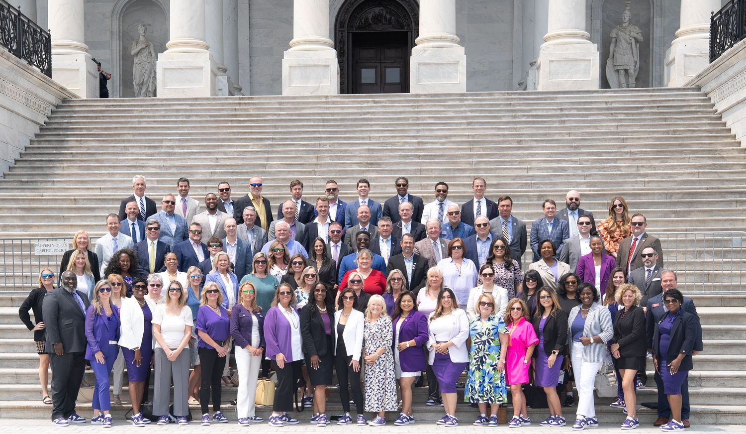 Large group of people gathered on the steps of a grand building with white columns and stone architecture.