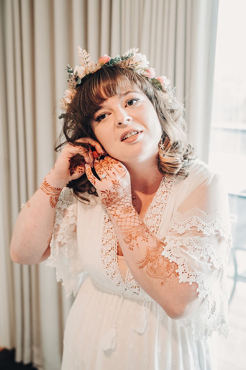 A dreamy bridal portrait showing a delicate lace dress and floral crown with soft natural window lighting.