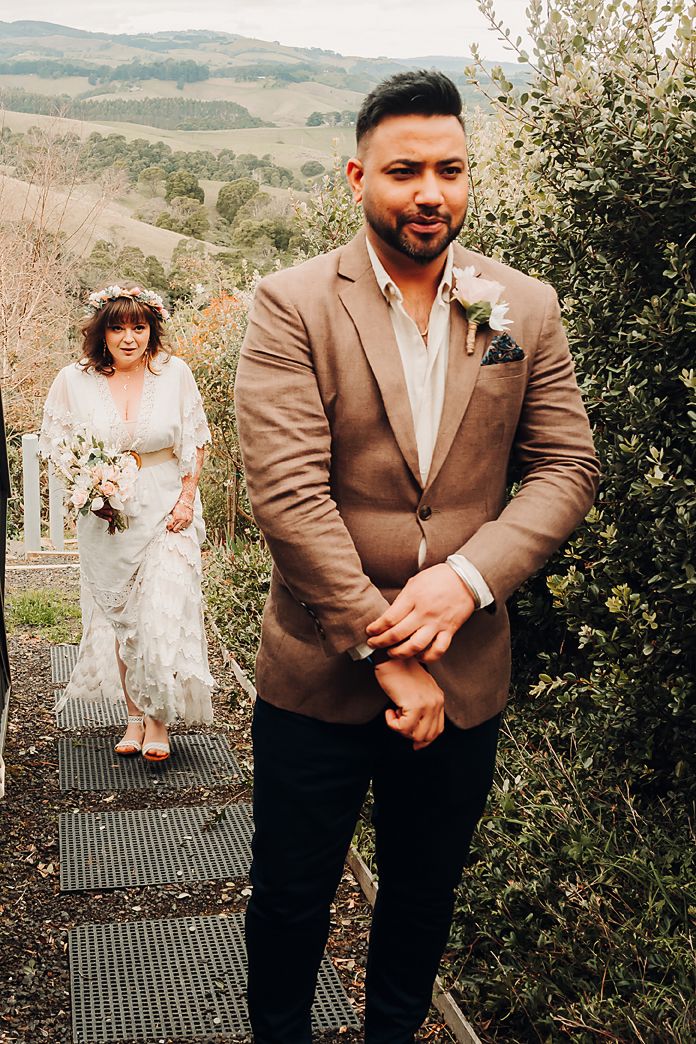 Wedding couple poses on garden steps with mountain views, bride in white lace and groom in tan suit jacket.
