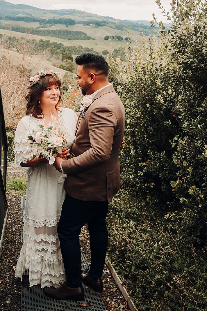 A couple shares romantic moments against a scenic mountain backdrop in brown and cream wedding attire.