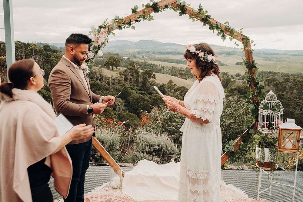 A romantic outdoor wedding ceremony under a floral arch with mountain views and rustic decor in the background.