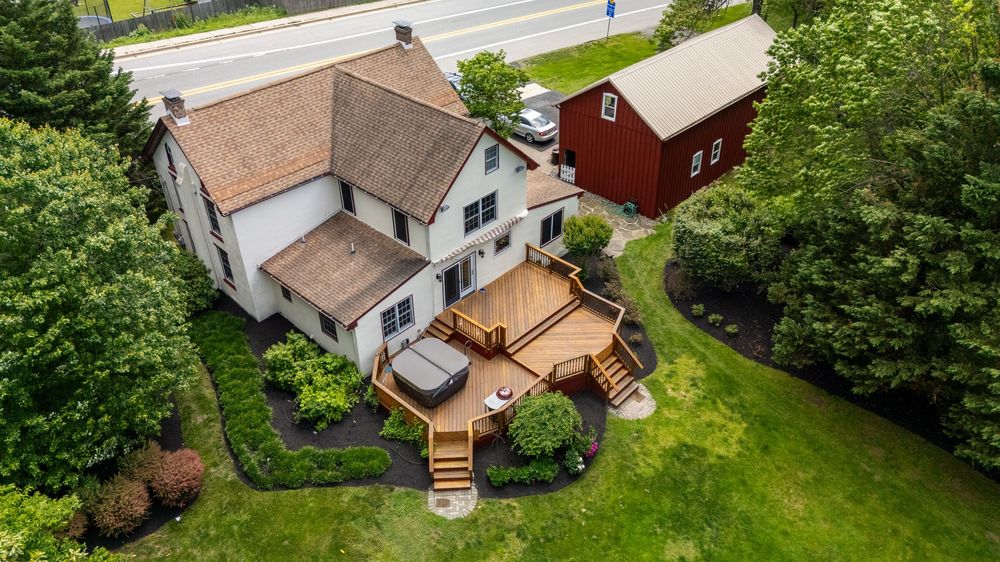 Aerial panoramic view of residential houses and backyards surrounded by green trees along a street.