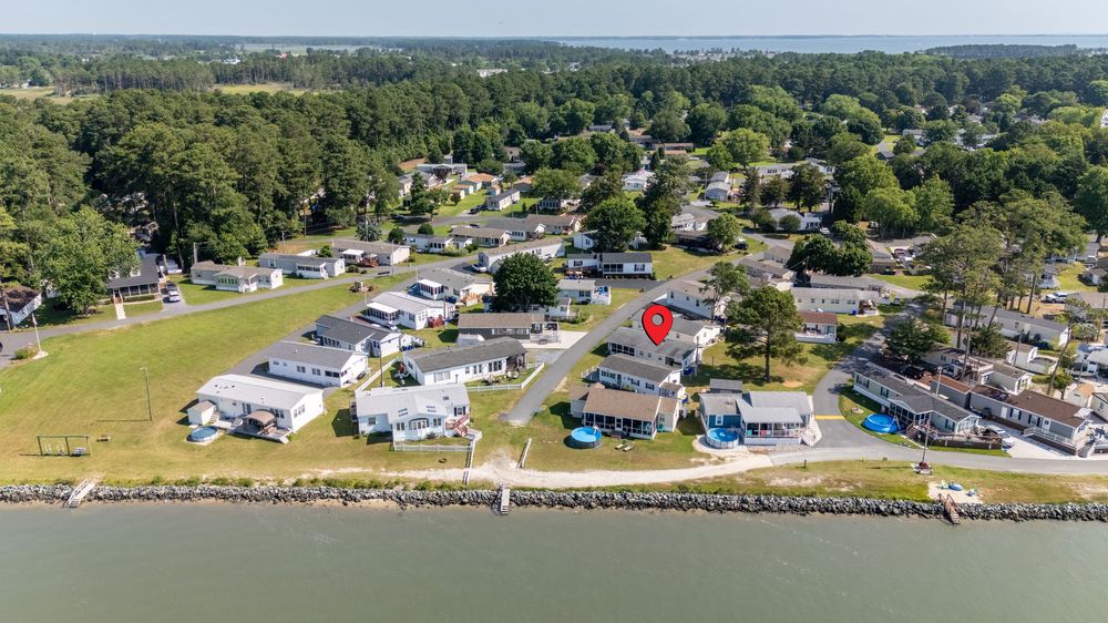 Aerial view of a coastal neighborhood with mobile homes and RVs along a seawall in a scenic waterfront location.