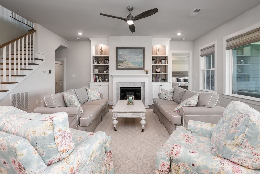 Elegant basement living area with built-in shelving, ceiling fan, and recessed lighting showcases a comfortable seating arrangement.