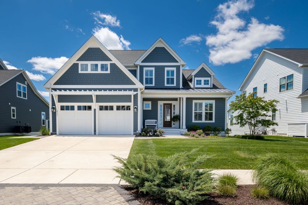 Beautiful two-story gray craftsman style home with white trim, double garage, and well-manicured lawn on sunny day.