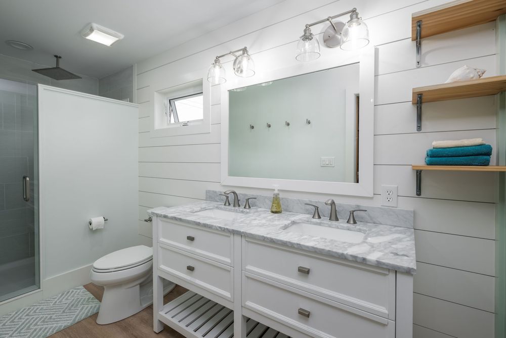 Modern white bathroom with shiplap walls, marble countertop double vanity, and wooden floating shelves.
