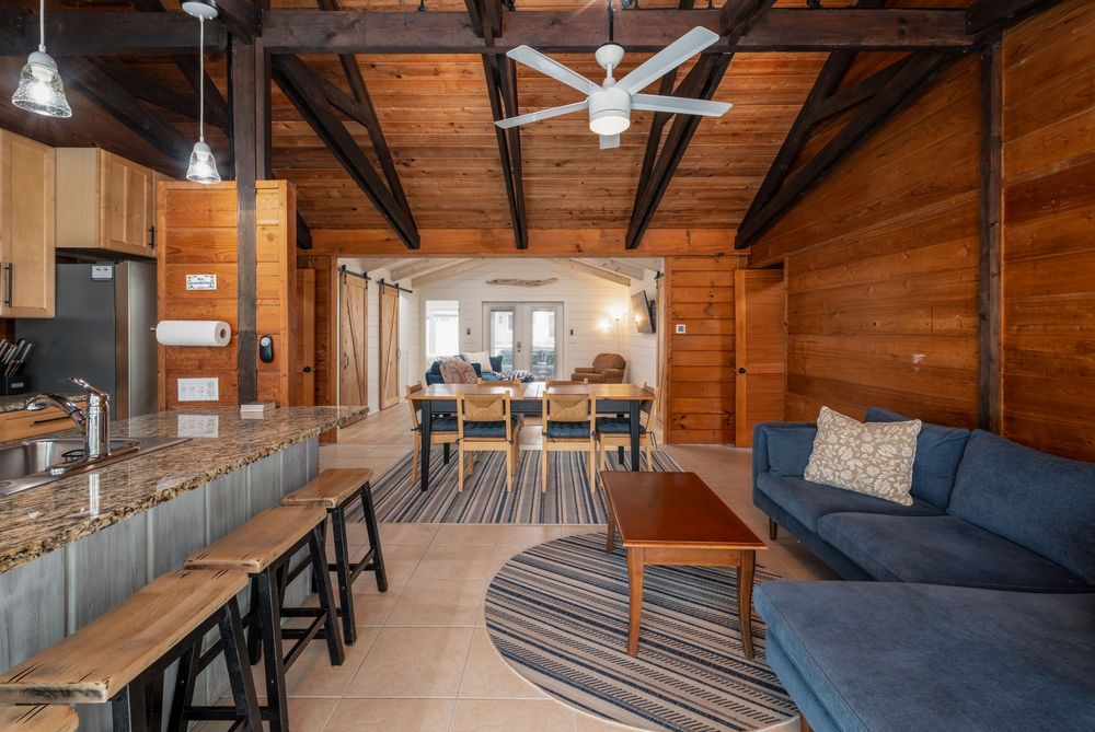 Modern cabin interior with exposed wood beams, white pendant lights, and sleek furnishings creates a cozy coastal retreat.
