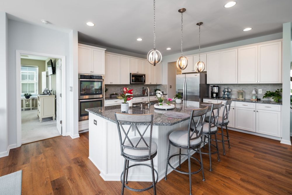 Modern open concept kitchen features white quartz countertops, pendant lights, and hardwood floors with transitional cabinets.