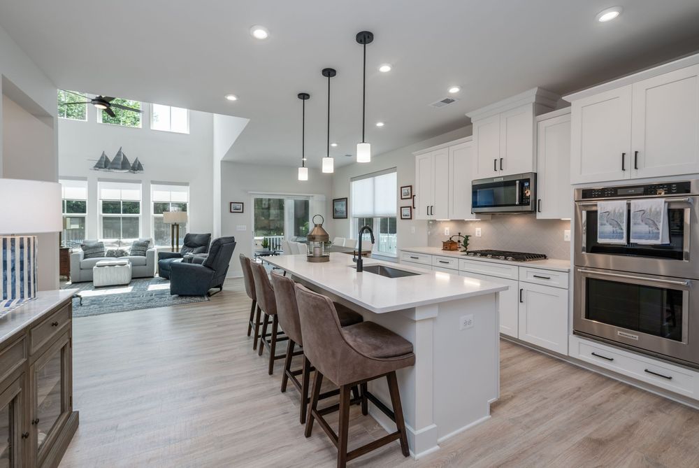 Modern open concept kitchen with white cabinets, quartz countertops, pendant lights and bar seating overlooking living room.