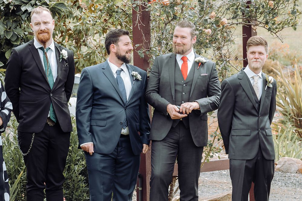 Groomsmen in formal suits standing together outdoors for a wedding photo.