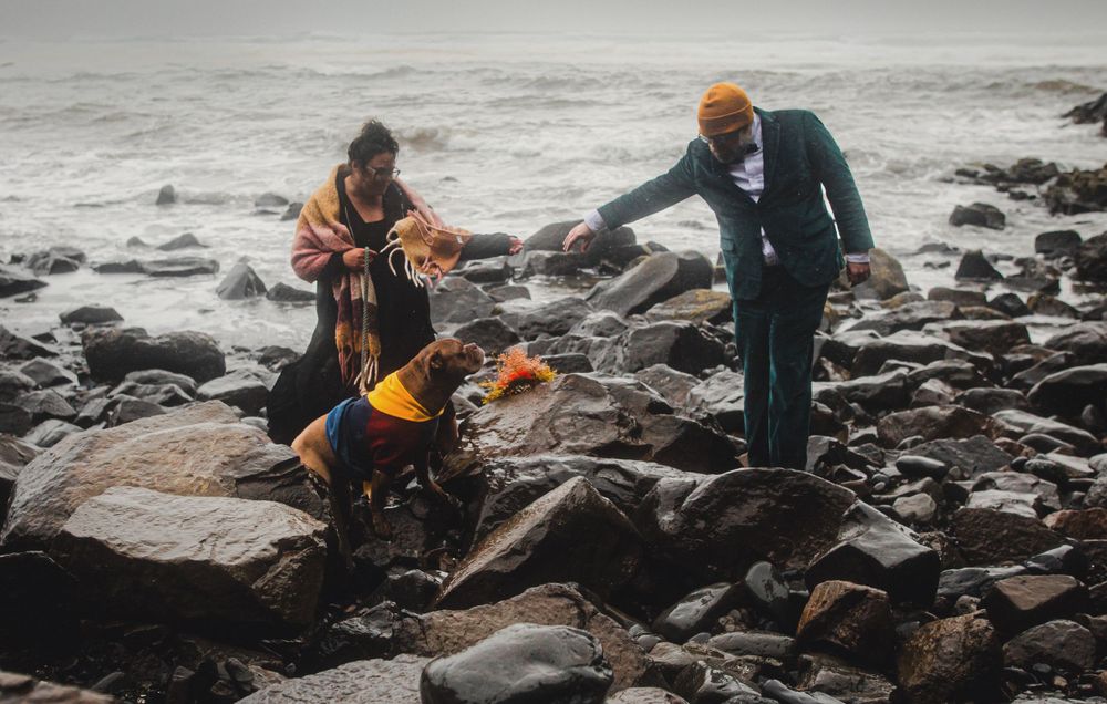 People carefully navigate large rocks on a rugged Pacific Northwest beach.