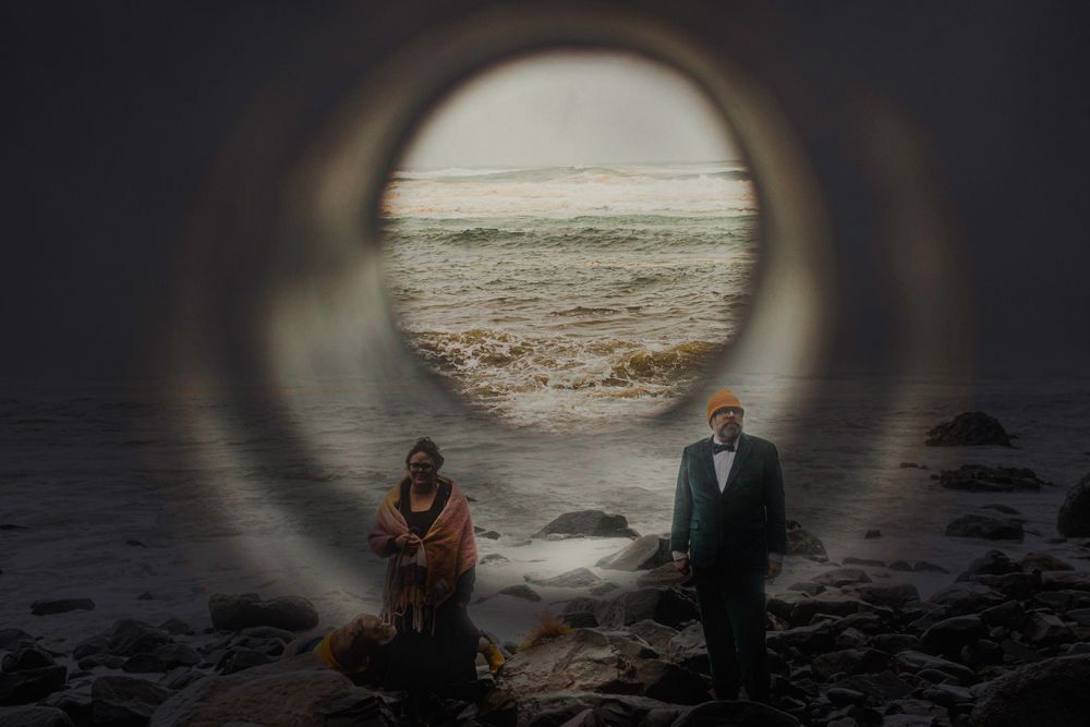 A circular framed view captures two figures standing on a rocky shoreline.