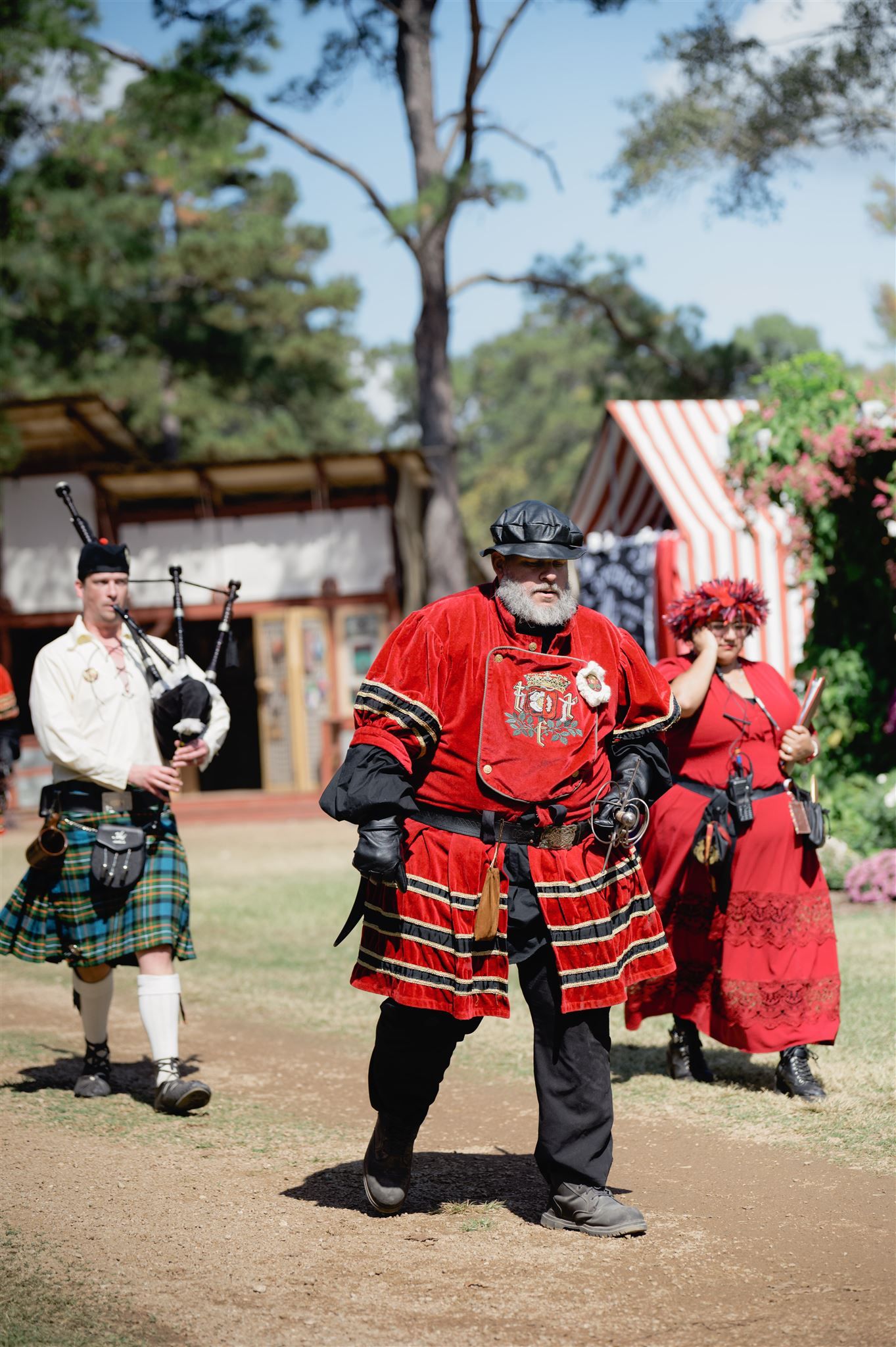 Performers in traditional Scottish and medieval costumes at a Renaissance festival with bagpipes and red attire.