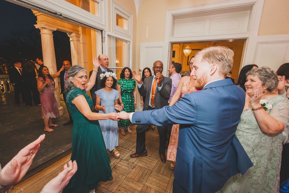Wedding guests dance together in a ballroom with colorful lighting and festive atmosphere during reception celebration.
