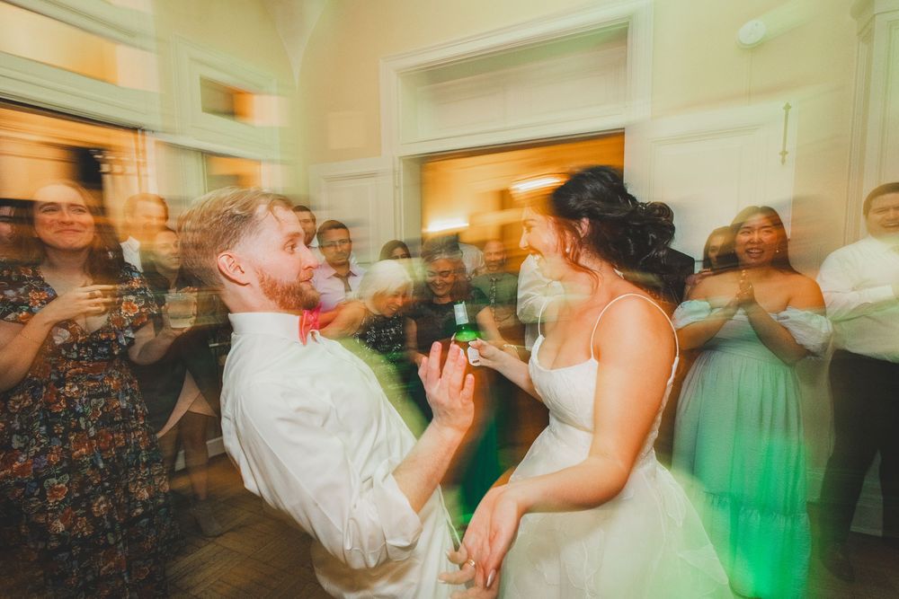 A couple shares an energetic moment on the dance floor at their wedding reception with guests in the background.