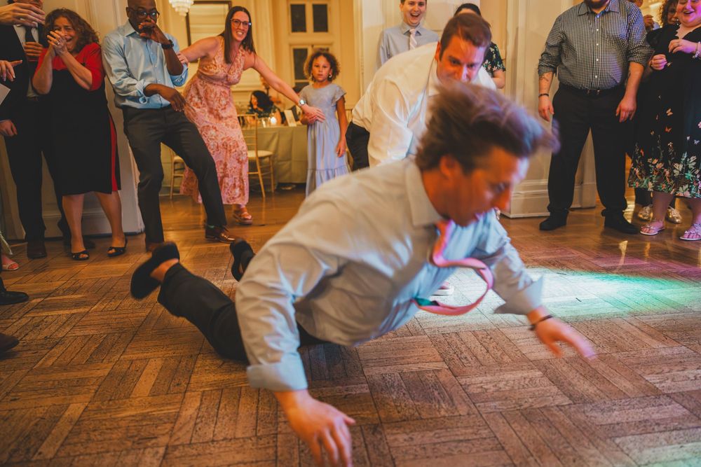 A lively wedding guest on their knees sliding across a wooden dance floor during a reception celebration.
