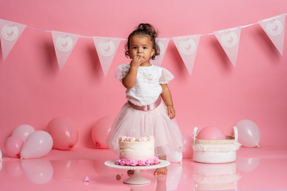Festive pink birthday setup with white bunting and birthday cake against a rosy backdrop.