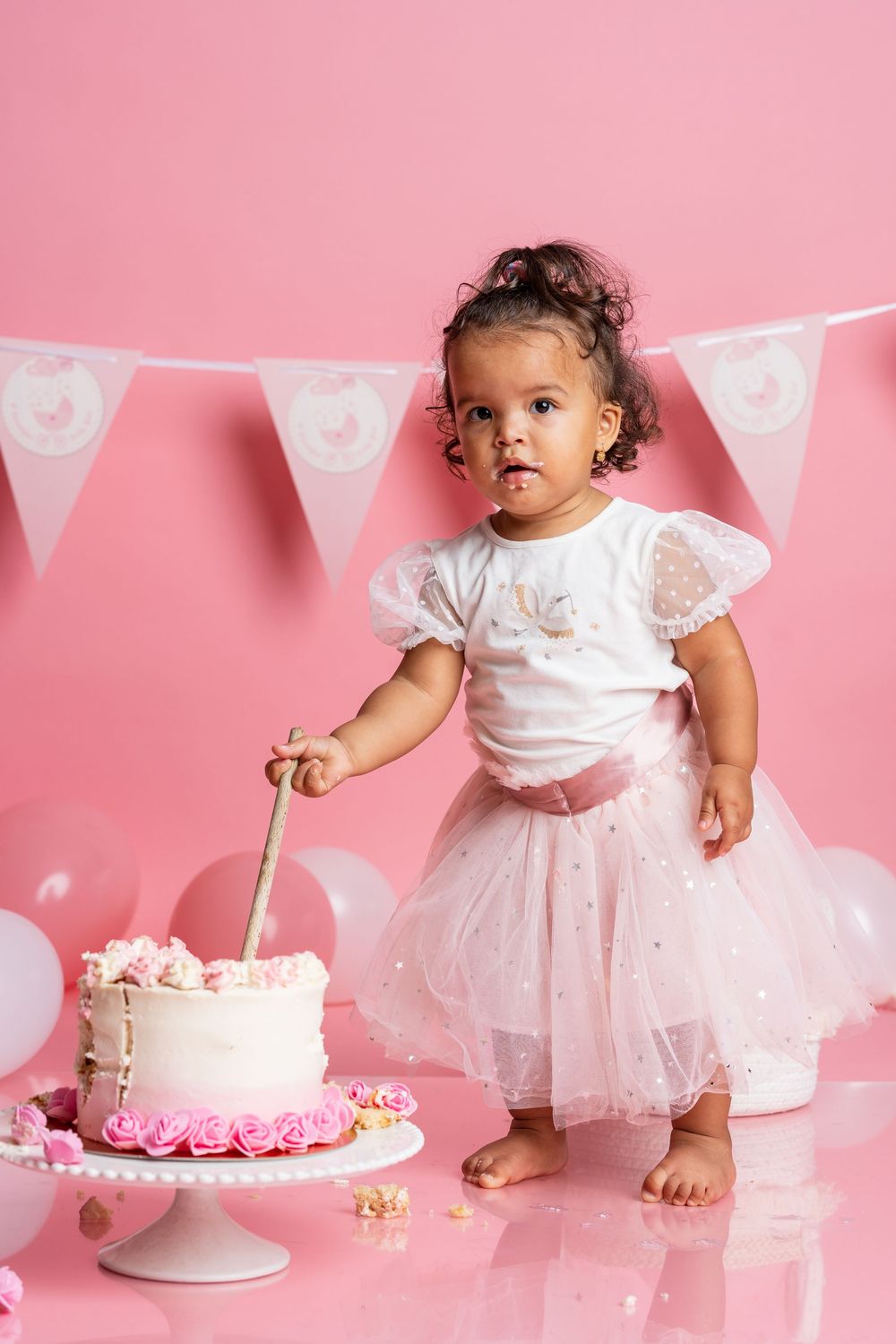 First birthday cake smash session with pink decorations featuring a white tutu dress and white cake with pink accents.
