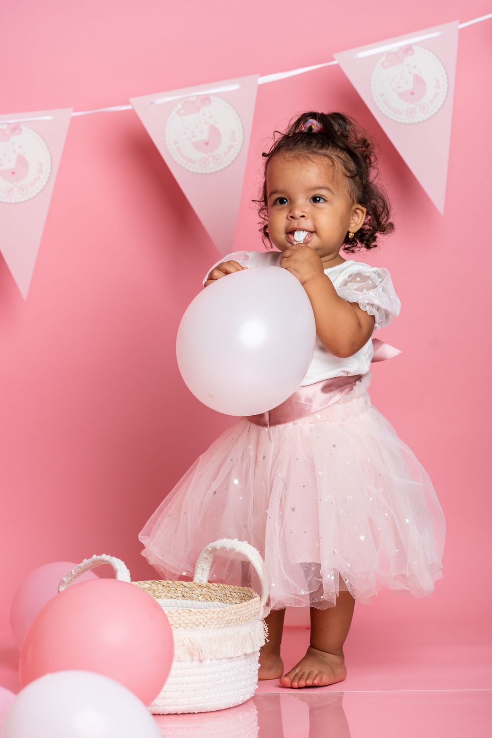 Happy child in tulle dress poses with white balloon against pink background with party decorations.