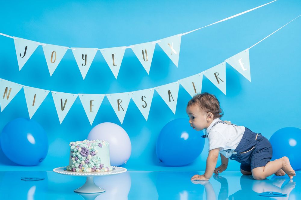 Birthday party setup with blue and white bunting, balloons, and decorative cake against bright turquoise backdrop.