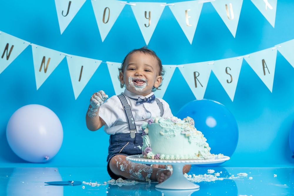 Joyful cake smash scene with frosting mess and celebration decorations against blue background.