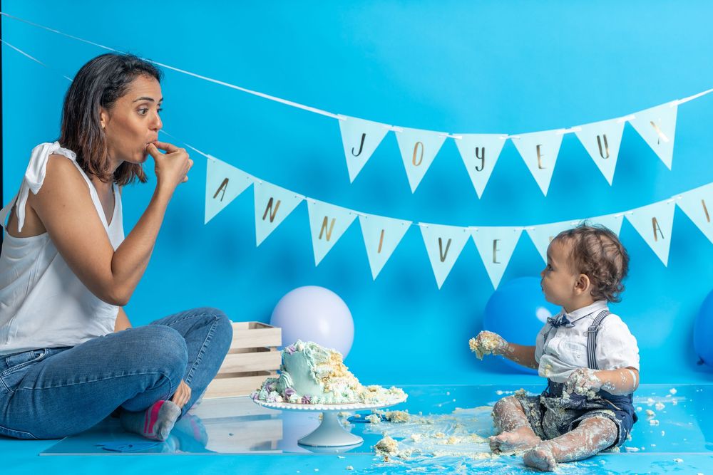 Fun cake smash photography session with blue and white party decorations and scattered frosting.