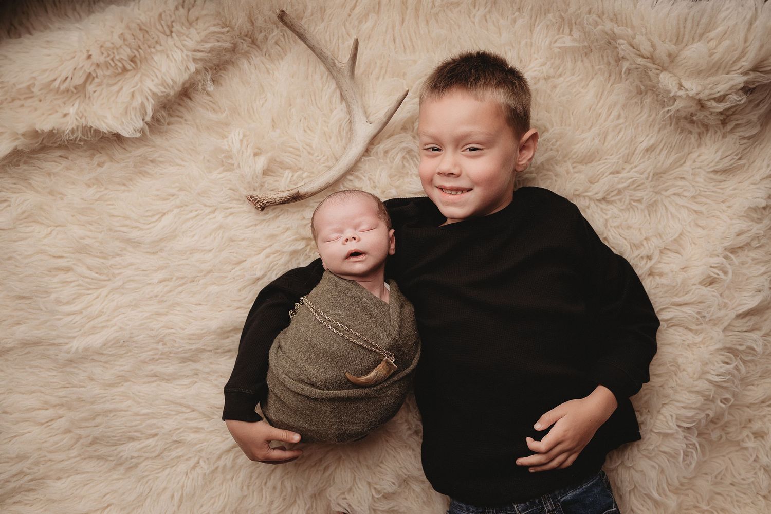 Professional photo of a newborn baby and his big brother in front of an antler