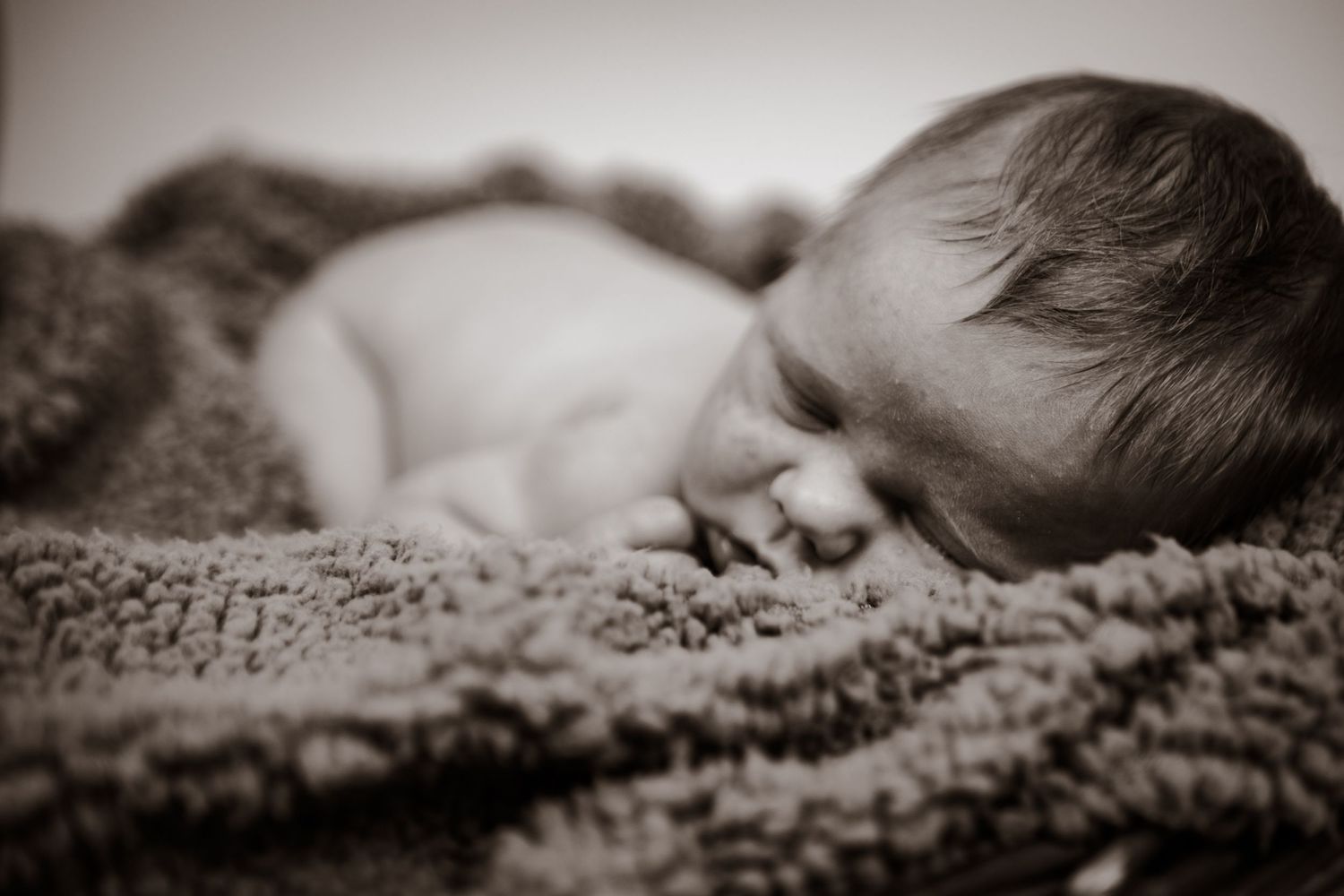 A sleeping baby wrapped in a cozy textured blanket photographed in black and white.