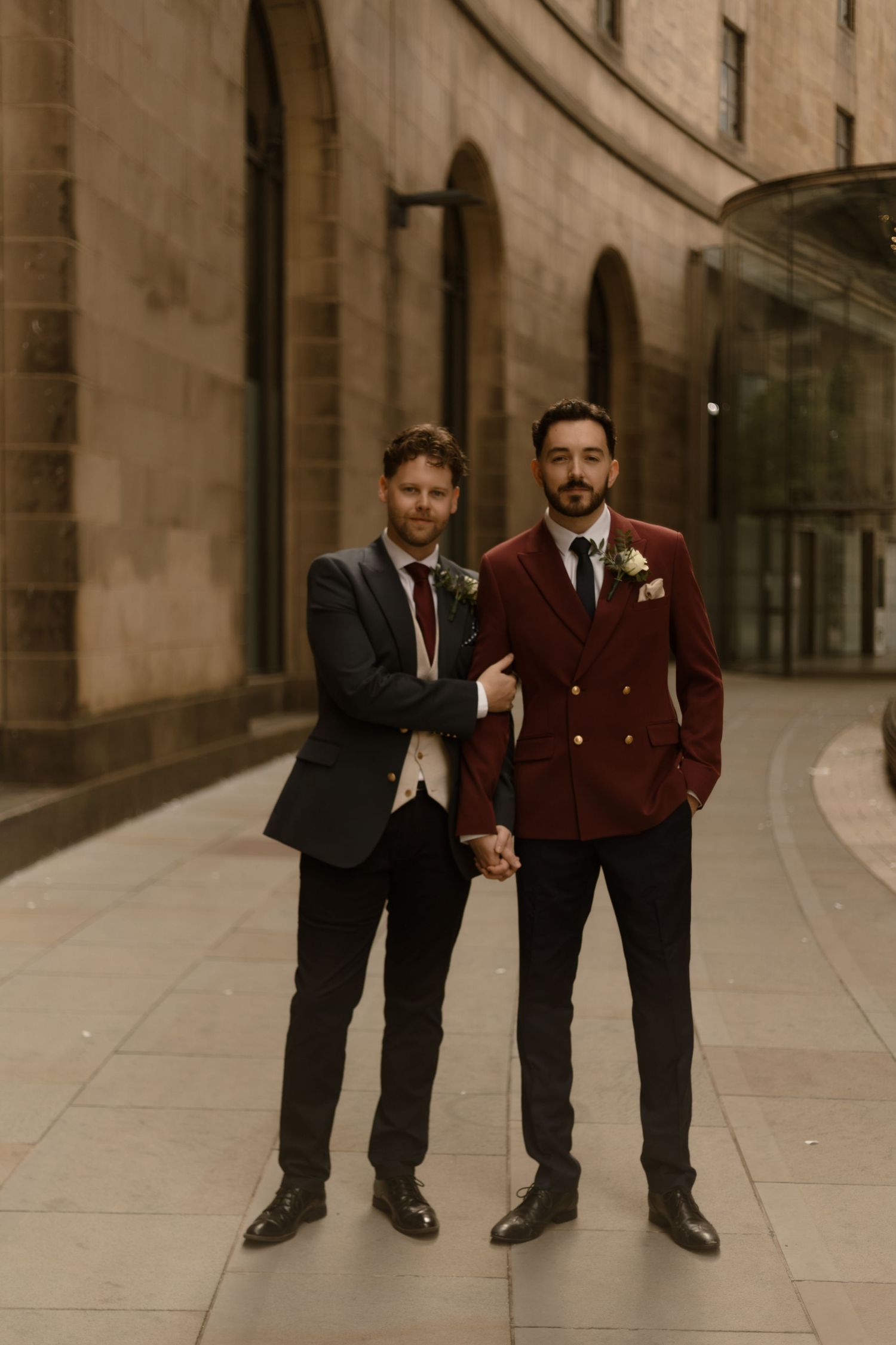 A cheerful wedding party celebrates on the grounds of a historic stone manor house in muted sepia tones.