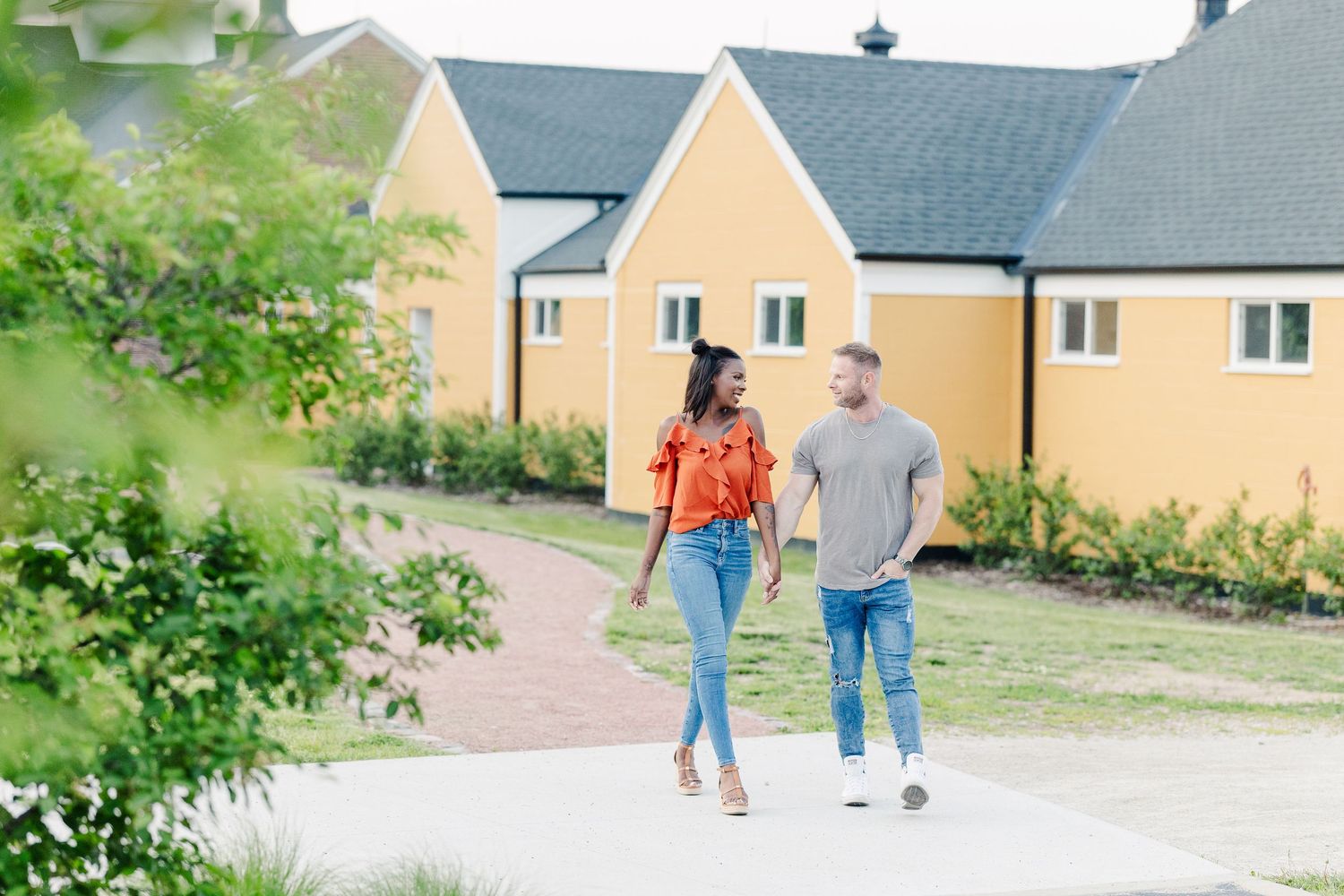 Two people walk together on a pathway beside beige townhouses on a pleasant spring day.